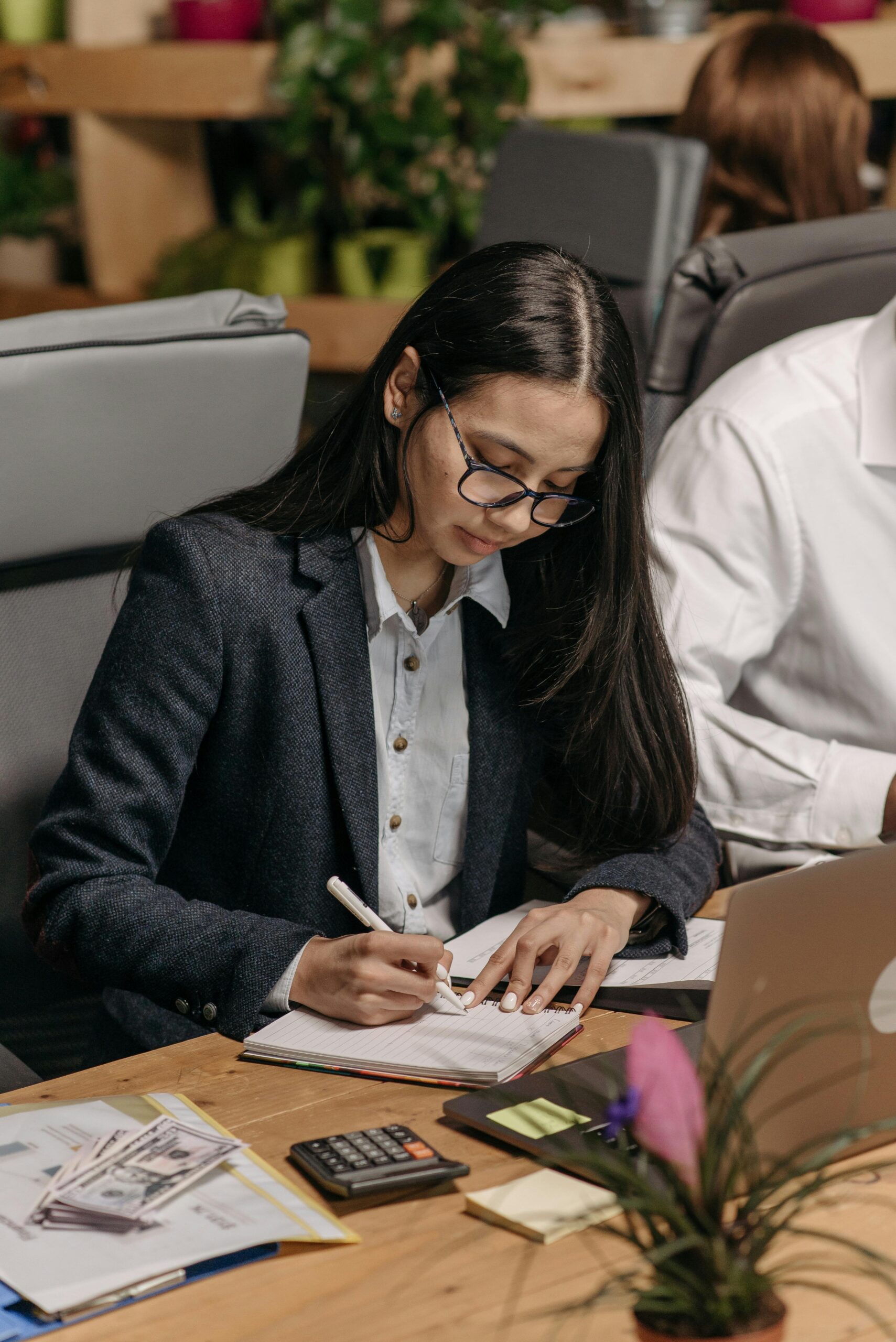 Young woman focused on writing notes at her desk in an office setting.