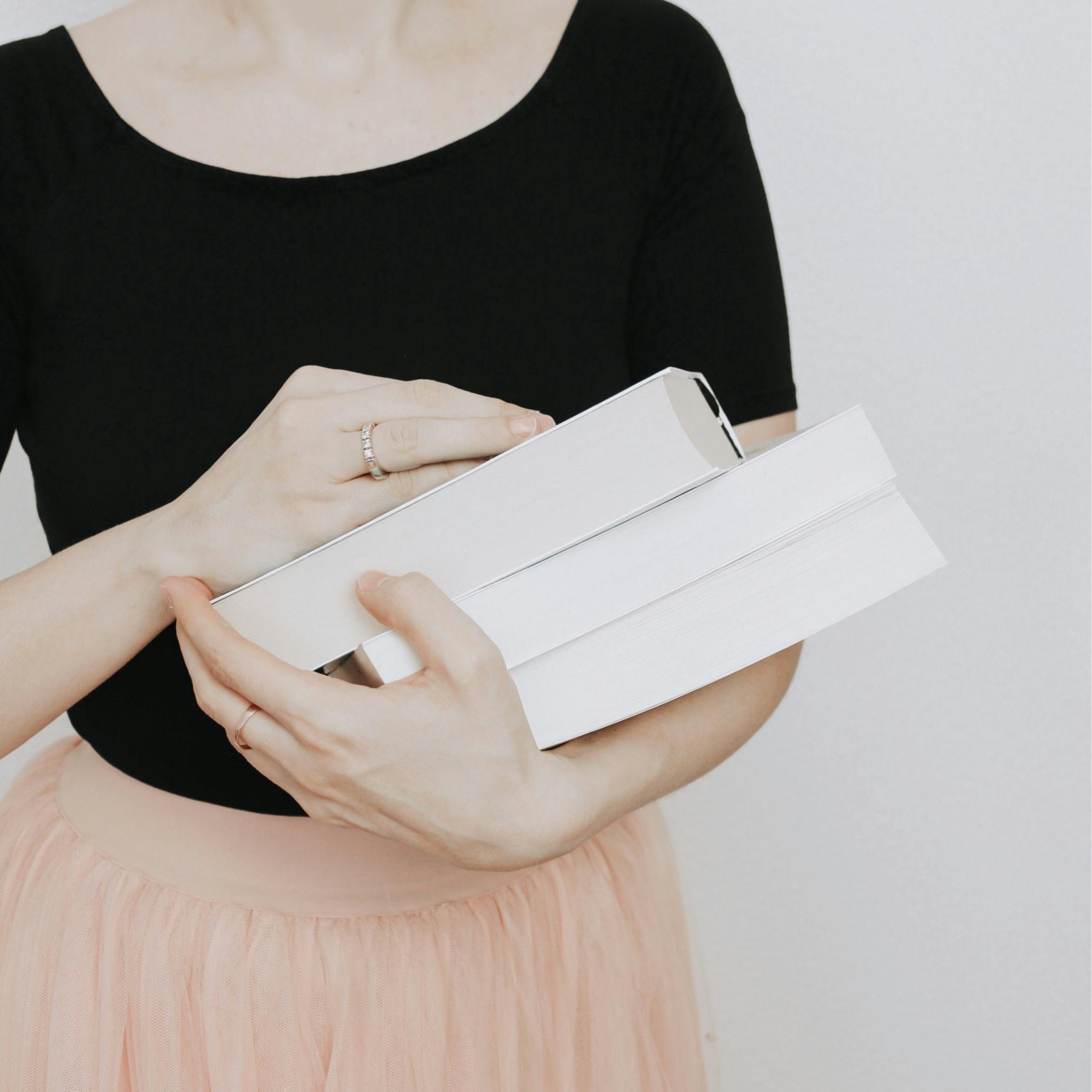 A woman in a black top and pink skirt holding white books, minimalist style.